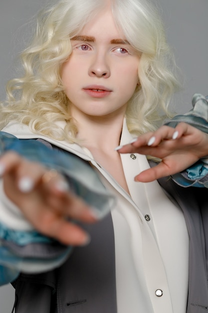 Mooi albino-meisje met een blanke huid, natuurlijke lippen en wit krullend haar, gekleed in een stijlvolle witte trui, close-up foto, kopieer ruimte