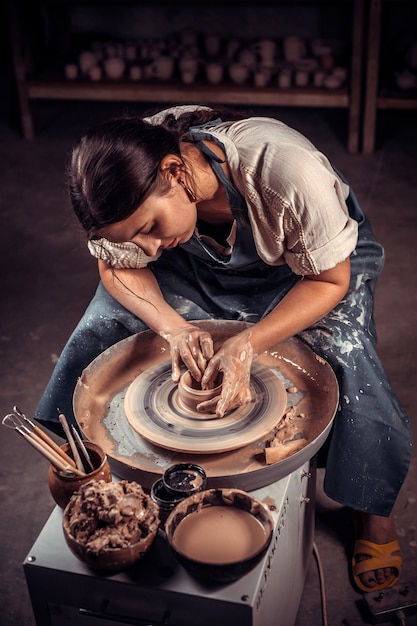 Mooi artisanaal meisje dat aardewerk, beeldhouwer van natte klei op wiel maakt.