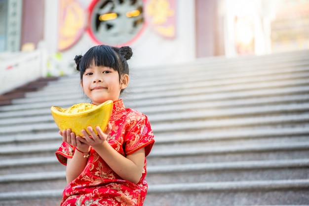 Mooi Aziatisch meisje draagt rode cheongsam en houdt Chinese goudstaaf voor de marmeren trappen van de prachtige Chinese tempel voor Chinees Nieuwjaar