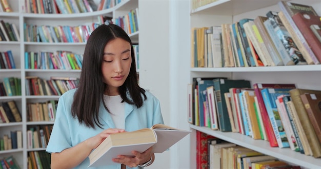 Mooi Aziatisch meisje in blauw shirt loopt langs de planken met boeken in het onderwijsconcept van de bibliotheek College