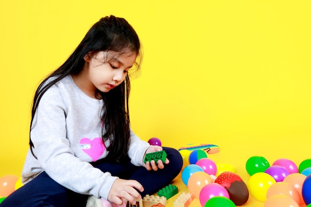 Mooi Aziatisch meisje op trui geniet van het spelen van kinderen om plastic blokken te monteren en te verbinden als grappig spel om creatieve verbeeldingskracht te tonen terwijl ze op schoolplein van kleurrijke ballen en speelgoed zitten