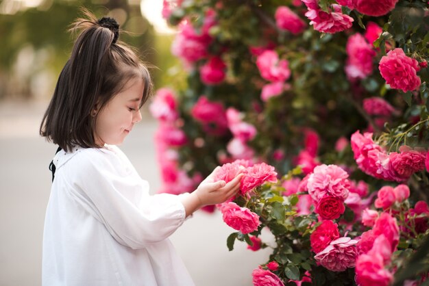 Mooi babymeisje die verse roze rozen in tuin houden