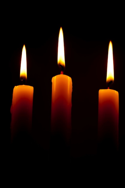Mooi beeld met 3 verlichte kaarsen met witte en geelachtige vlammen op een zwarte achtergrond