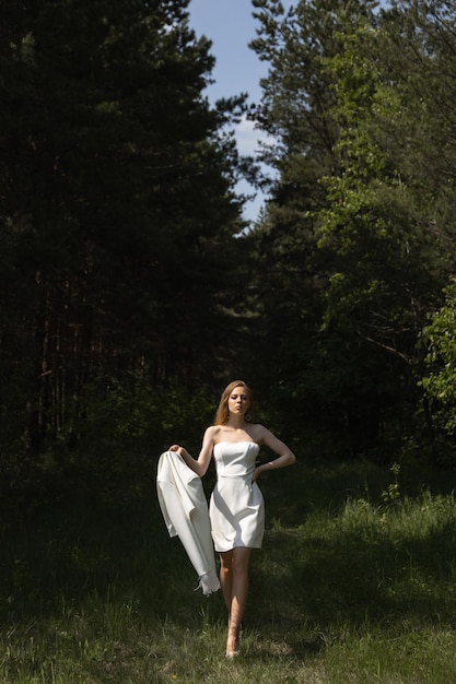 Foto mooi blank blond meisje in een wit trouwpak in het bos