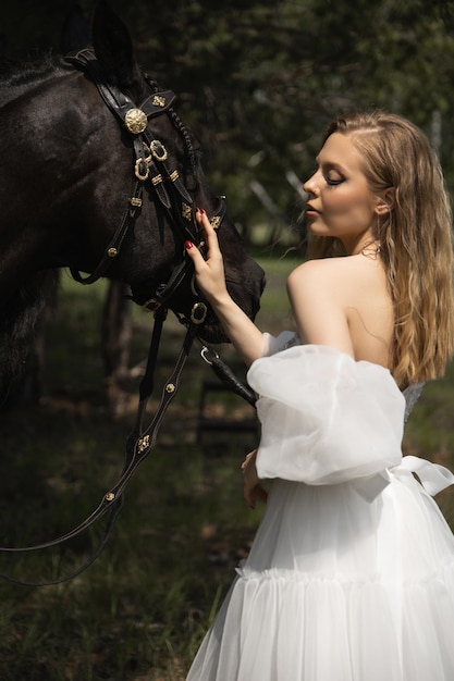 Foto mooi blank meisje in een trouwjurk aait een paard in het gezicht