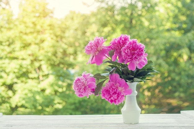 Mooi bleek - roze pioenenboeket in witte vaas over aard groene achtergrond.