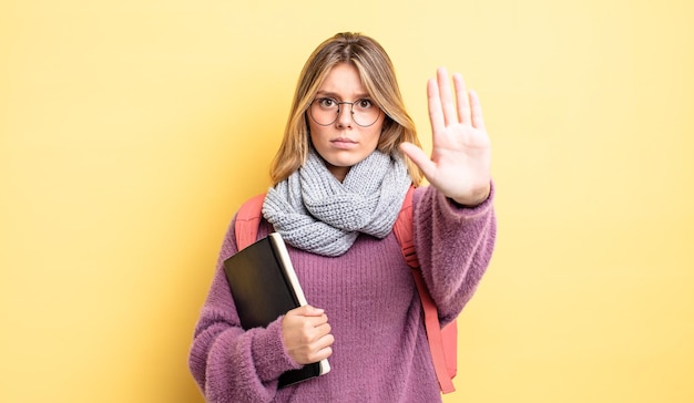 Mooi blond meisje dat er serieus uitziet en een open palm toont die een stopgebaar maakt. studentenconcept