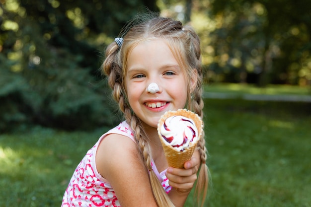 Mooi blond meisje dat ijs eet in de zomer in het park. vrolijk meisje met ijs.