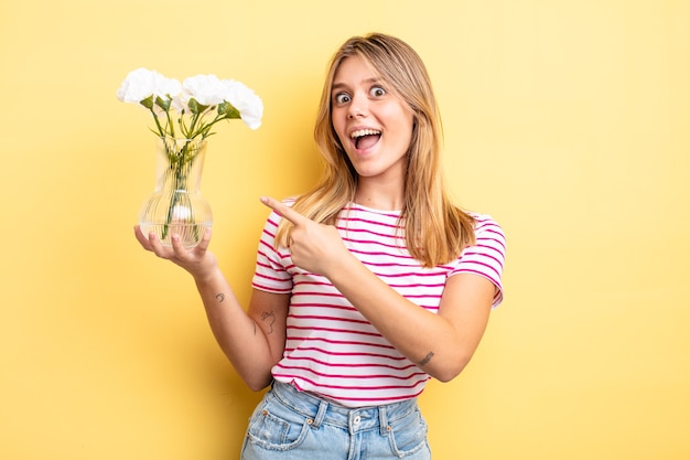 Foto mooi blond meisje dat opgewonden en verrast kijkt en naar de zijkant wijst. decoratief bloemenconcept