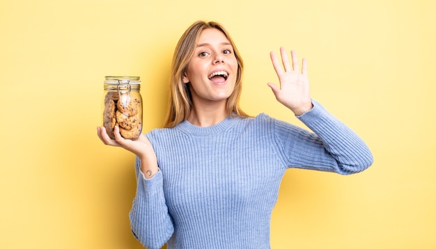 Mooi blond meisje dat vrolijk lacht, met de hand zwaait, je verwelkomt en begroet. zelfgemaakte koekjes concept