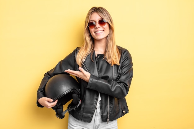 Mooi blond meisje dat vrolijk lacht, zich gelukkig voelt en een concept toont. motorhelm concept