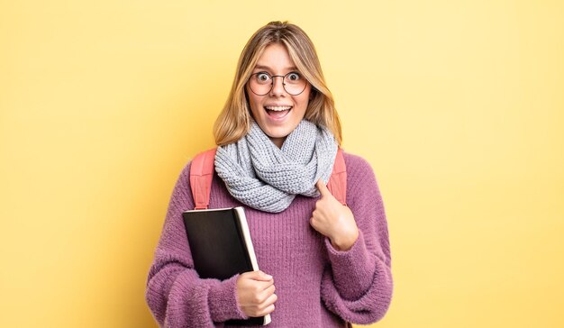 Mooi blond meisje dat zich gelukkig voelt en naar zichzelf wijst met een opgewonden studentenconcept