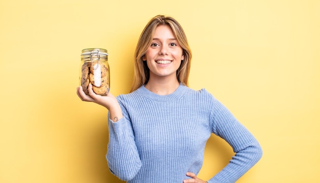 Mooi blond meisje glimlachend gelukkig met een hand op de heup en zelfverzekerd. zelfgemaakte koekjes concept