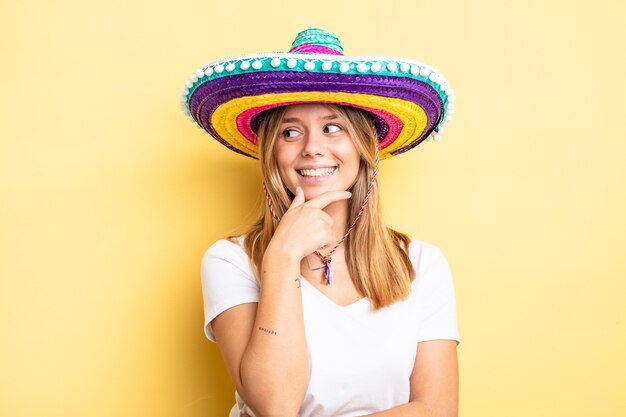 mooi blond meisje glimlachend met een gelukkige, zelfverzekerde uitdrukking met de hand op de kin. mexicaanse hoed concept