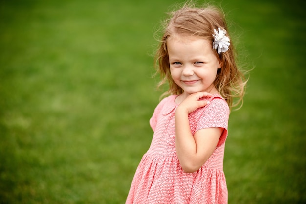 Mooi blond meisje in een roze jurk staande op het groene gras in de zomer