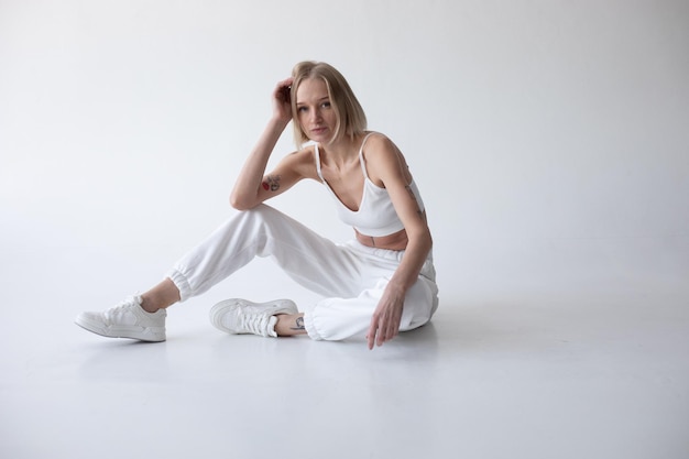 Foto mooi blond meisje in een witte top en collets poseert op een witte achtergrond