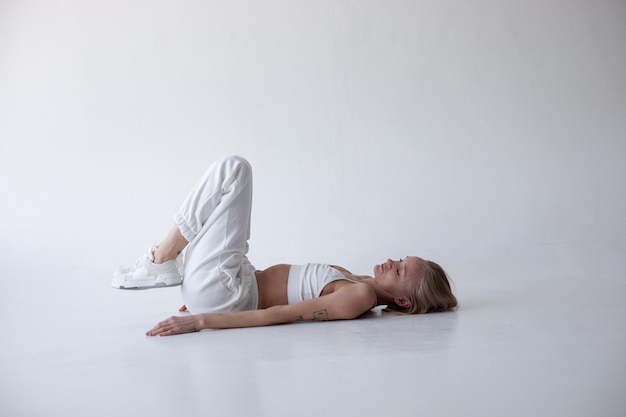 Foto mooi blond meisje in een witte top en strikjes poseert op een witte achtergrond op de vloer