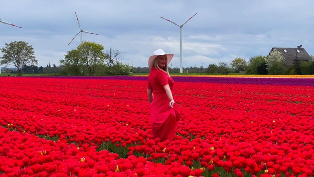 Mooi blond meisje in rode jurk en witte strohoed met rieten mand op kleurrijke tulpenvelden