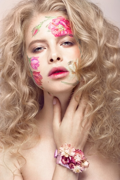 Mooi blond meisje met krullen en een bloemmotief op het gezicht. Schoonheid bloemen.