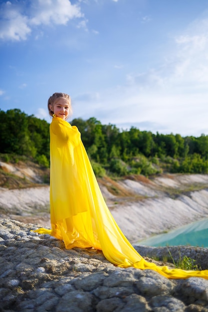 Mooi blond meisje poseren in een gele jurk in de natuur. zomer foto. blauwe lucht. zonnige dag.