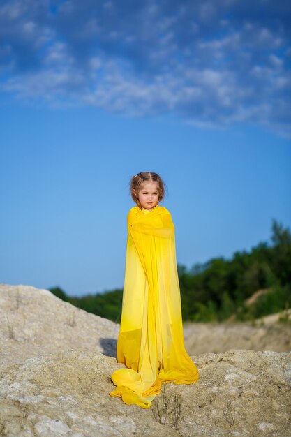 Mooi blond meisje poseren in een gele jurk in de natuur. Zomer foto. Blauwe lucht. Zonnige dag.