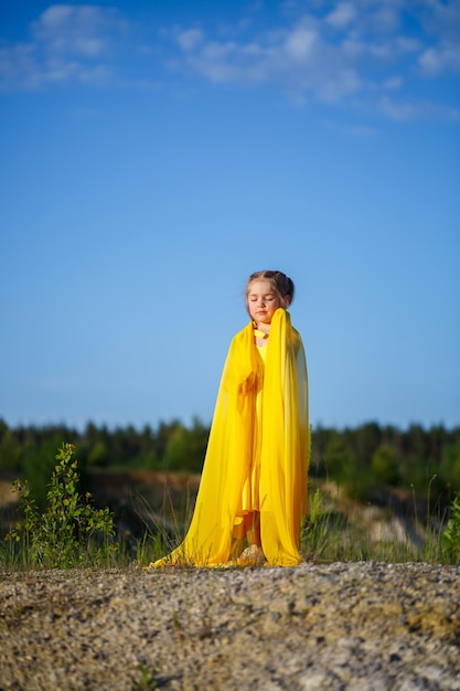 Mooi blond meisje poseren in een gele jurk in de natuur. Zomer foto. Blauwe lucht. Zonnige dag.