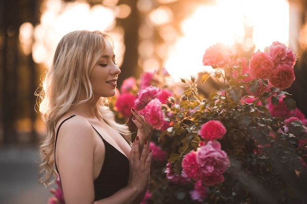 Mooi blond meisje poseren met roze rozen over zonsondergang