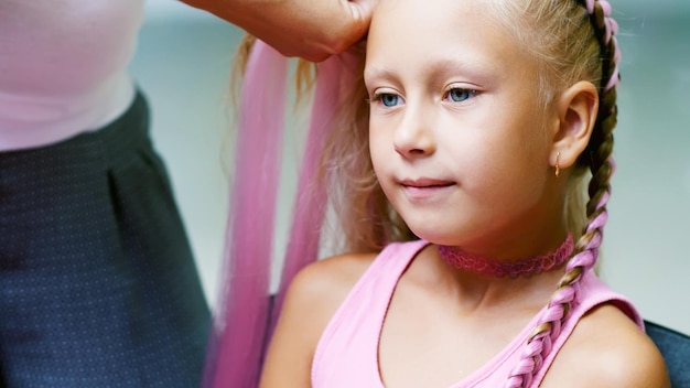 Foto mooi blond meisje van zeven jaar oud gevlochten twee pigtails doen een kapsel met roze lokken van