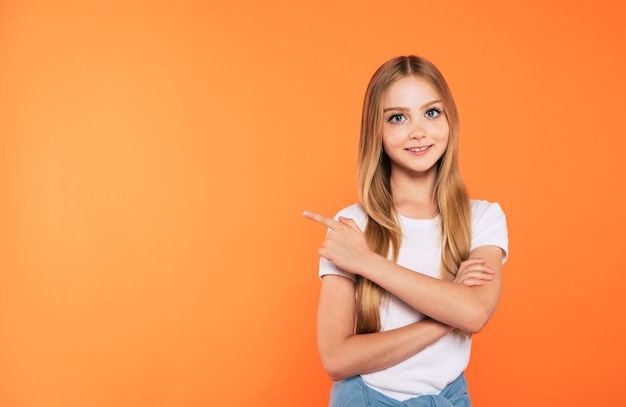 Mooi blond meisje wijst en laat iets zien in een wit t-shirt geïsoleerd op een gele muur in de studio