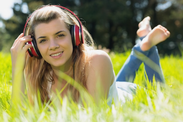 Mooi blonde die op gras liggen die aan muziek luisteren