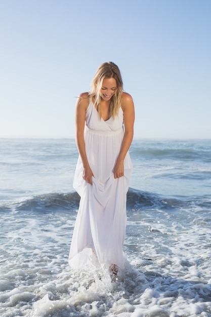 Mooi blonde die zich in het overzees bij het strand in witte sundress bevinden