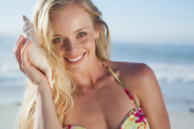 Mooi blonde in bikini die aan kroonslak op het strand luistert