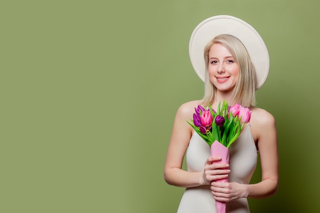 Mooi blondemeisje in witte hoed en kleding met tulpen