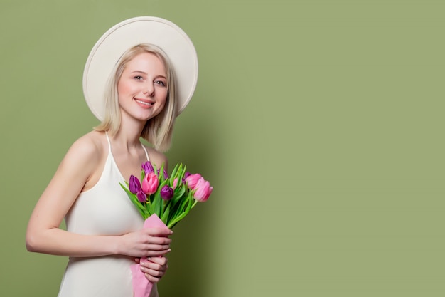 Mooi blondemeisje in witte hoed en kleding met tulpen