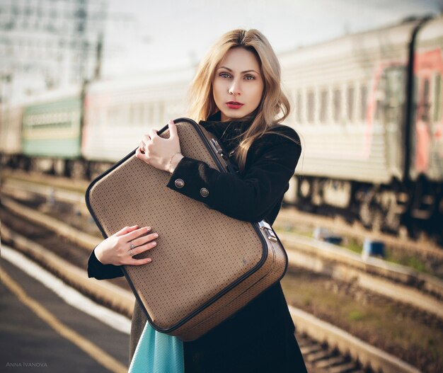 Foto mooi blondemeisje met een koffer die op een trein bij het station wachten