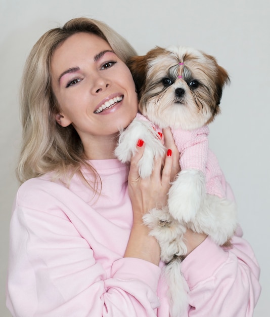 Mooi blondemeisje met een leuk puppy van shihtzu in roze kleren op een lichte achtergrond