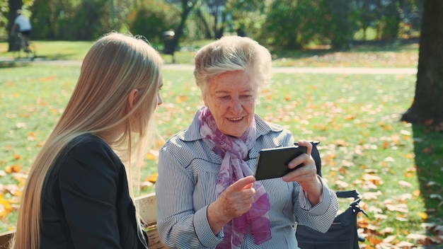 Foto mooi blondemeisje met oudere vrouwenzitting op bank en kijkend iets op smartphone