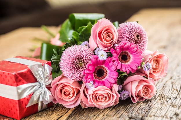 Mooi boeket bloemen met rode cadeau op houten tafel.