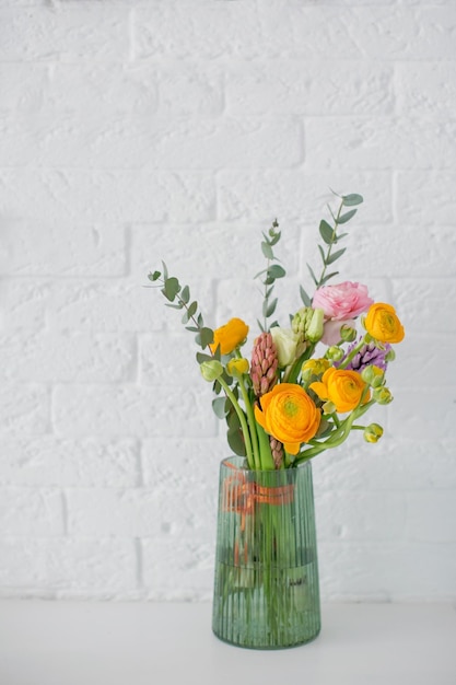 Mooi boeket met oranje en roze ranunculus bloemen eucalyptus en hyacint in een groene vaas op een witte achtergrond