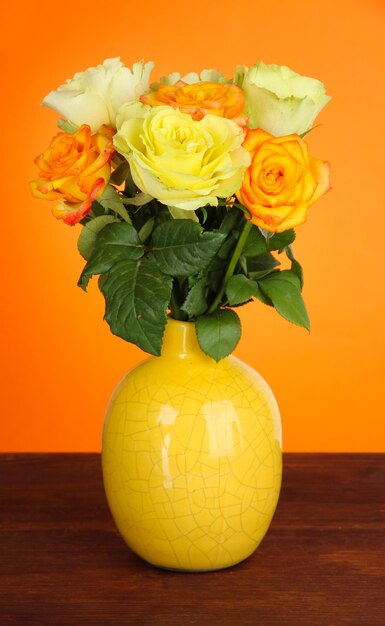 Mooi boeket rozen in vaas op tafel op oranje achtergrond