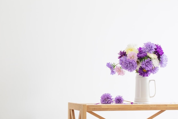 Mooi boeket van asters in witte kruik op witte muur als achtergrond