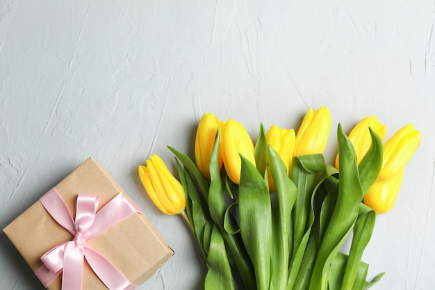 Mooi boeket van gele tulpen met cadeau op grijs, bovenaanzicht. Ruimte voor tekst