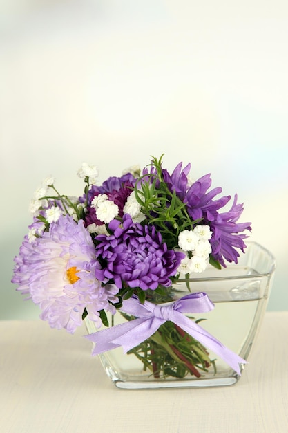 Mooi boeket van heldere bloemen in glazen vaas op houten tafel op lichte achtergrond