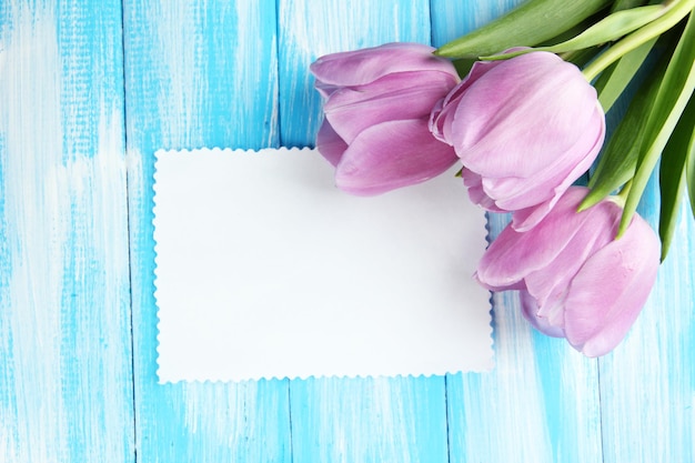 Mooi boeket van paarse tulpen en blanco kaart op blauwe houten achtergrond