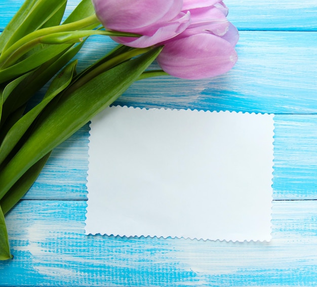 Mooi boeket van paarse tulpen en blanco kaart op blauwe houten achtergrond