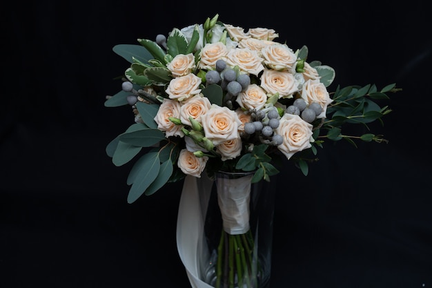 Mooi bruidsboeket van bossige roomroos, eucalyptus, Brunei, Pittosporum en Lisianthus op een zwarte muur.