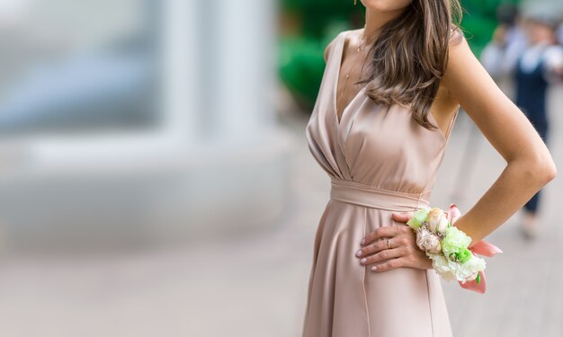 Mooi bruidsmeisje in een zijden jurk met een bloem corsages op haar hand tegen een groene tuin