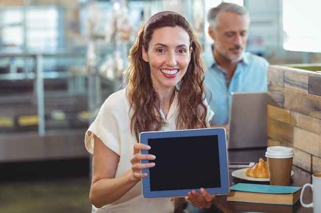 Mooi brunette die camera bekijken en tablet tonen