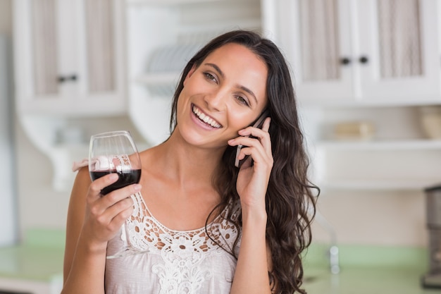 Mooi brunette op de telefoon die glas wijn hebben