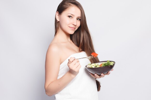 Mooi donkerbruin meisje dat in handdoek verse salade eet